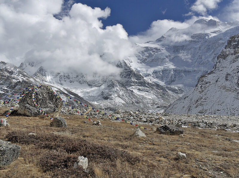 Kanchenjunga peak glowing orange at sunrise above dark forested ridges with prayer flags, Kanchenjunga Circuit Trek