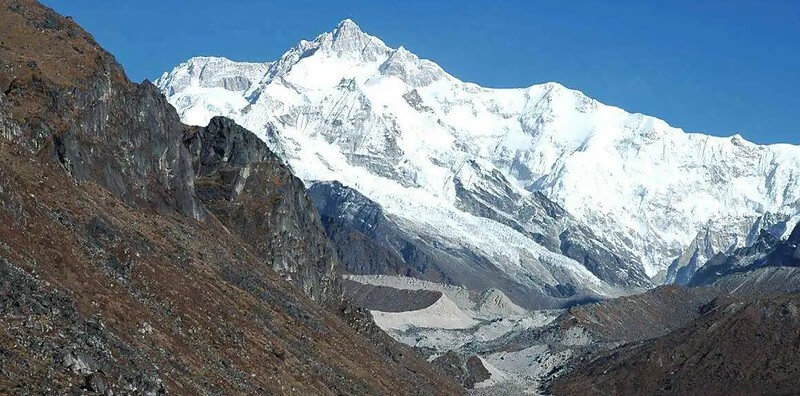 Snow-covered Kanchenjunga summit above a glacier and rugged brown slopes in the Nepal Himalaya